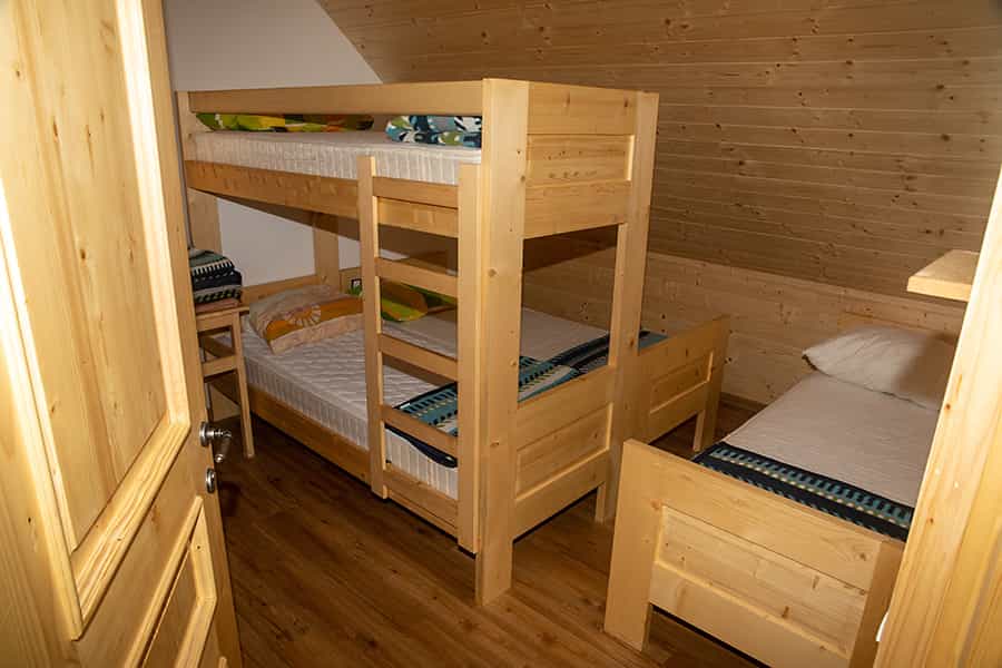 Wooden bunk beds and single bed inside an attic room with wood paneling and flooring.