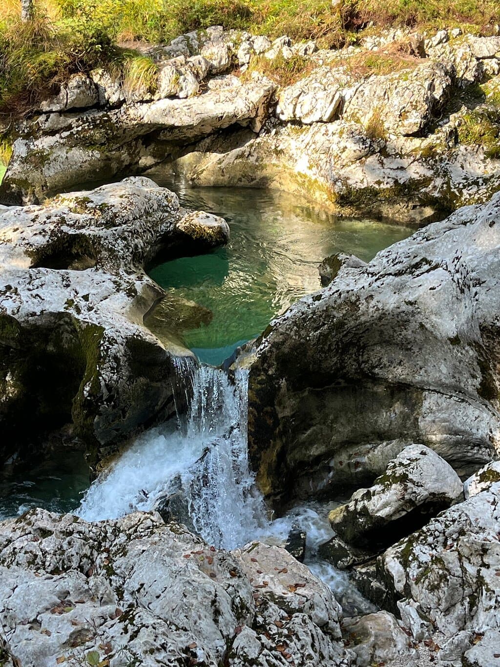 Small waterfall cascading over mossy rocks into a pool of clear, turquoise water.