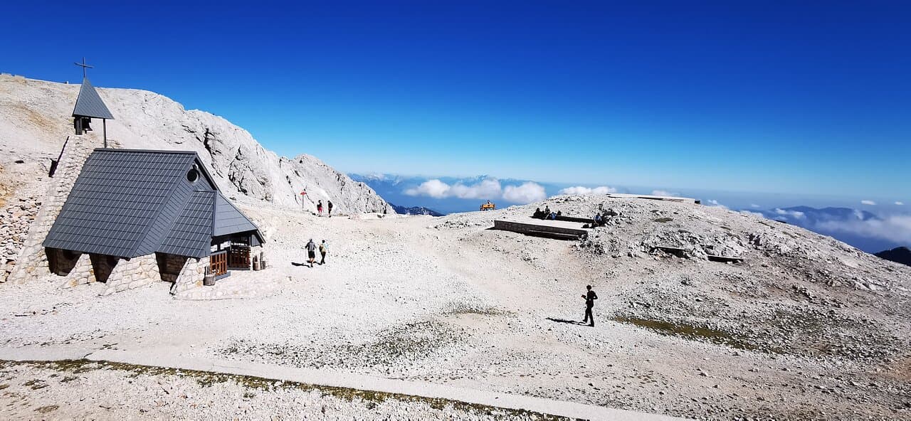 Stone chapel with bell tower on barren mountain summit under clear blue sky