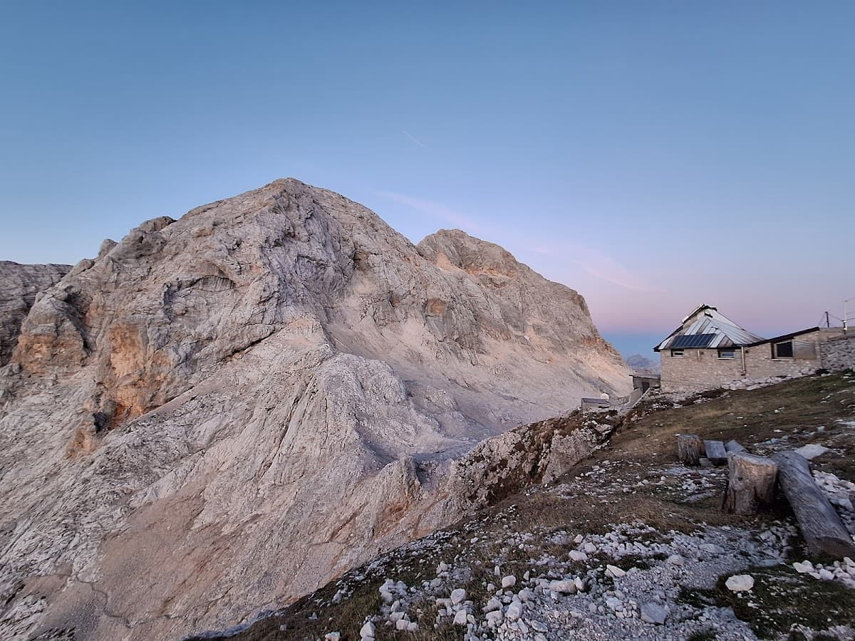 Stone mountain hut near massive rocky peak under clear blue and pink twilight sky