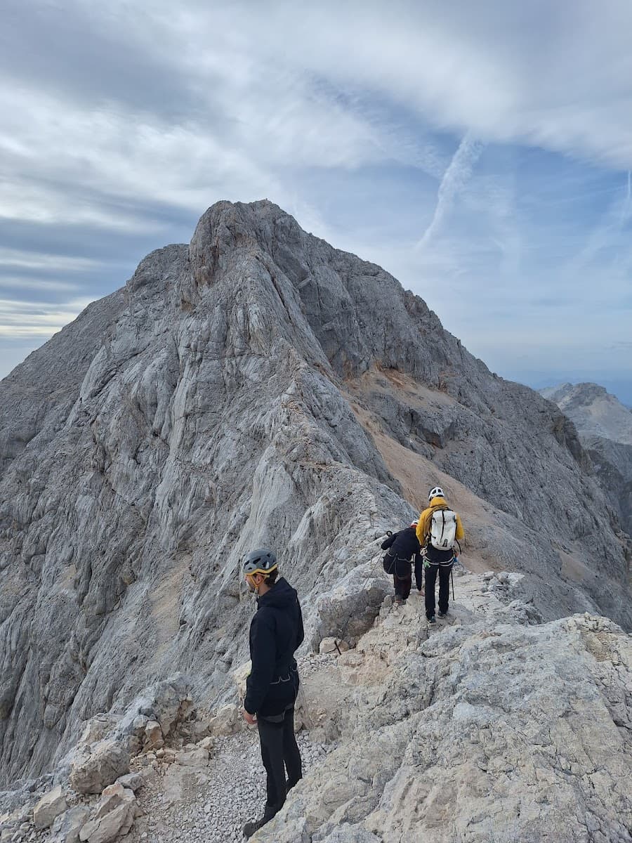 Hikers with helmets traversing a rocky mountain ridge under a cloudy sky