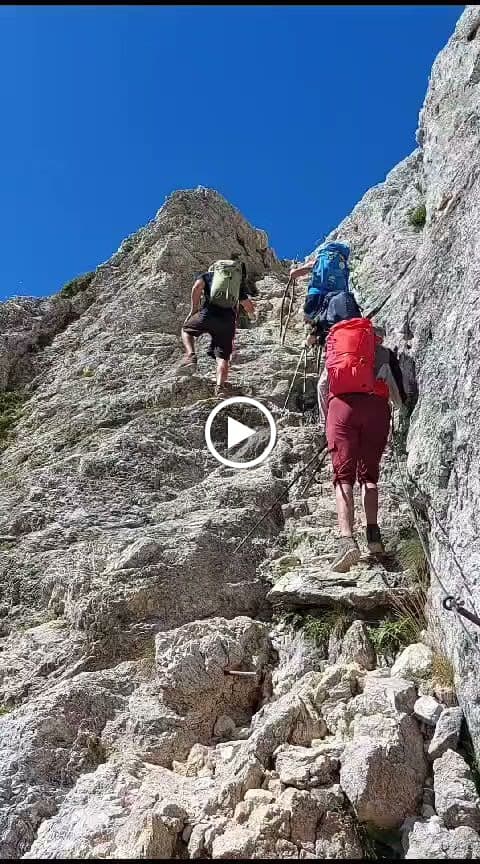 Hikers with backpacks ascending steep, rocky mountain terrain under a clear blue sky.