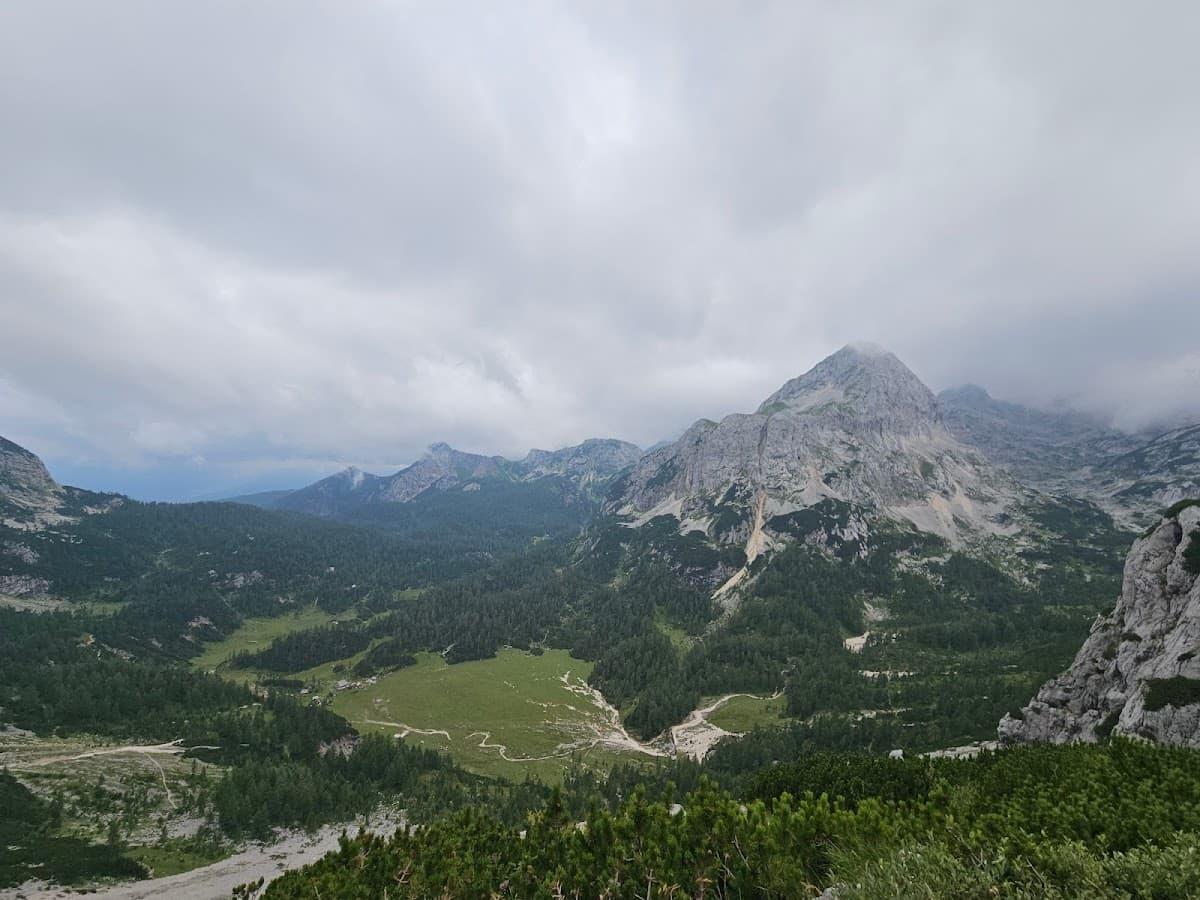 Rugged mountains under cloudy sky overlooking a forested valley with a small clearing.