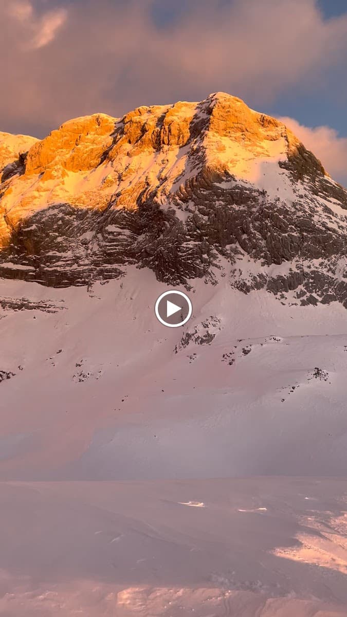 Snowy mountain peak illuminated by golden sunset light above vast snowfield