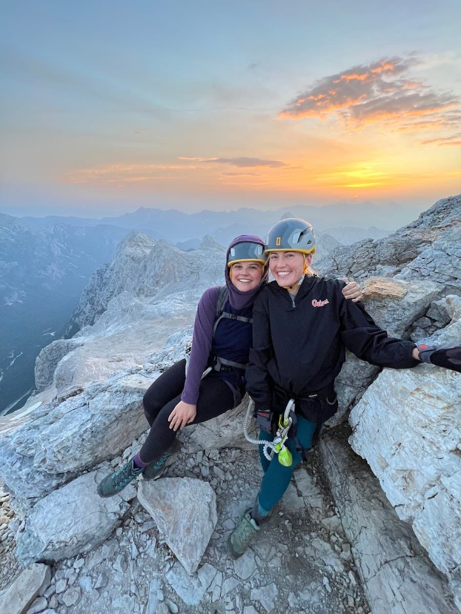 Two climbers resting on rocky mountain summit at sunset with hazy peaks in background