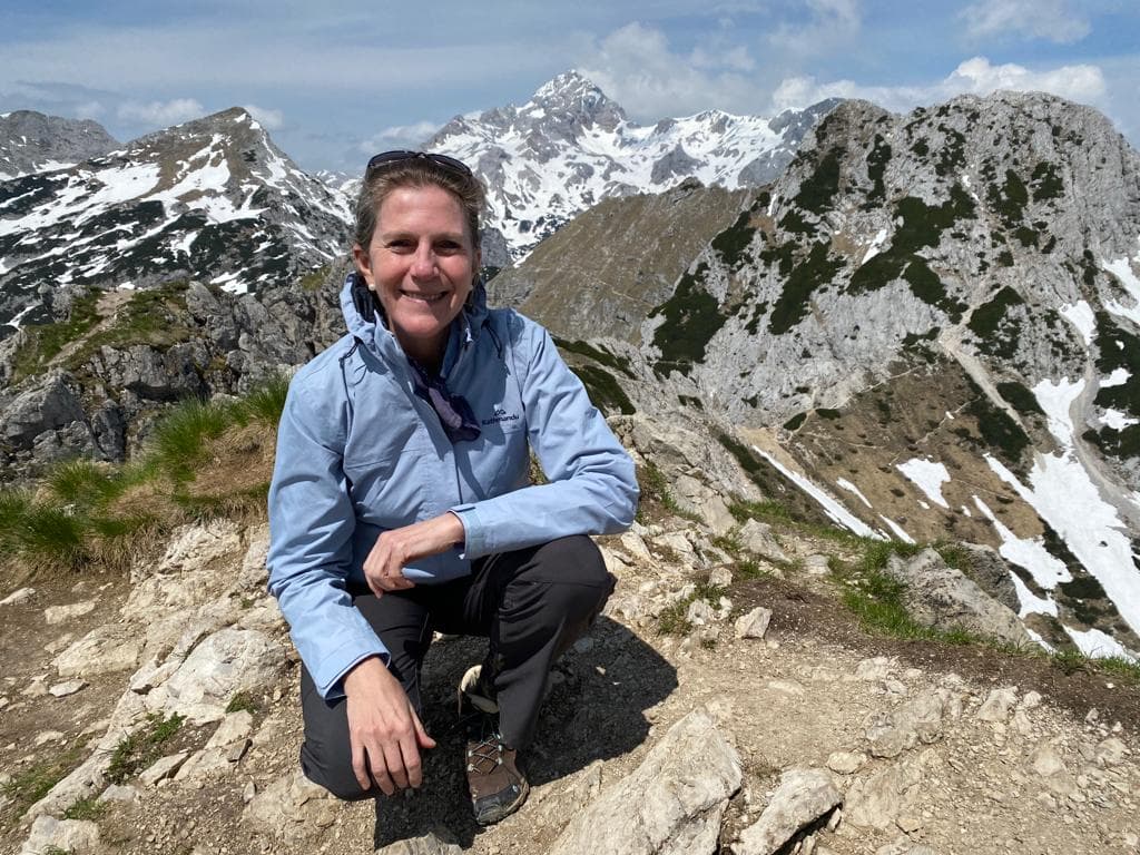 Hiker resting on rocky trail with snow-capped mountains in the background