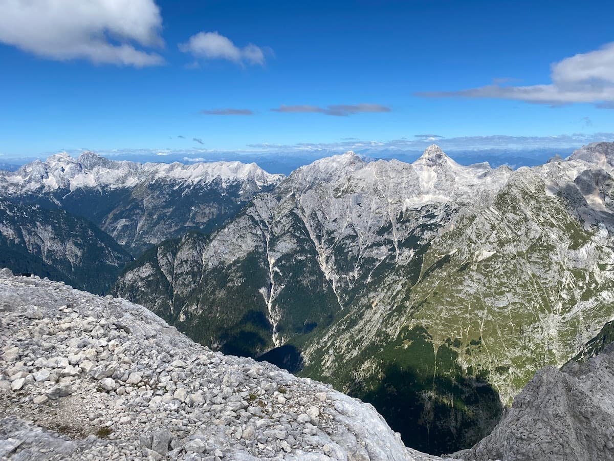 Rocky foreground overlooking vast alpine mountain range under a bright blue sky