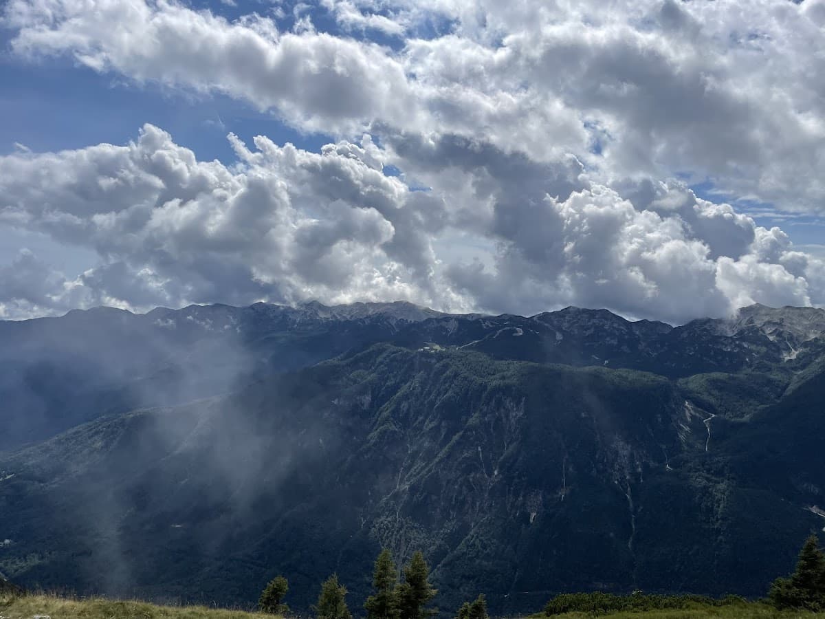 Mountain range with dark forested slopes under dramatic white clouds and blue sky