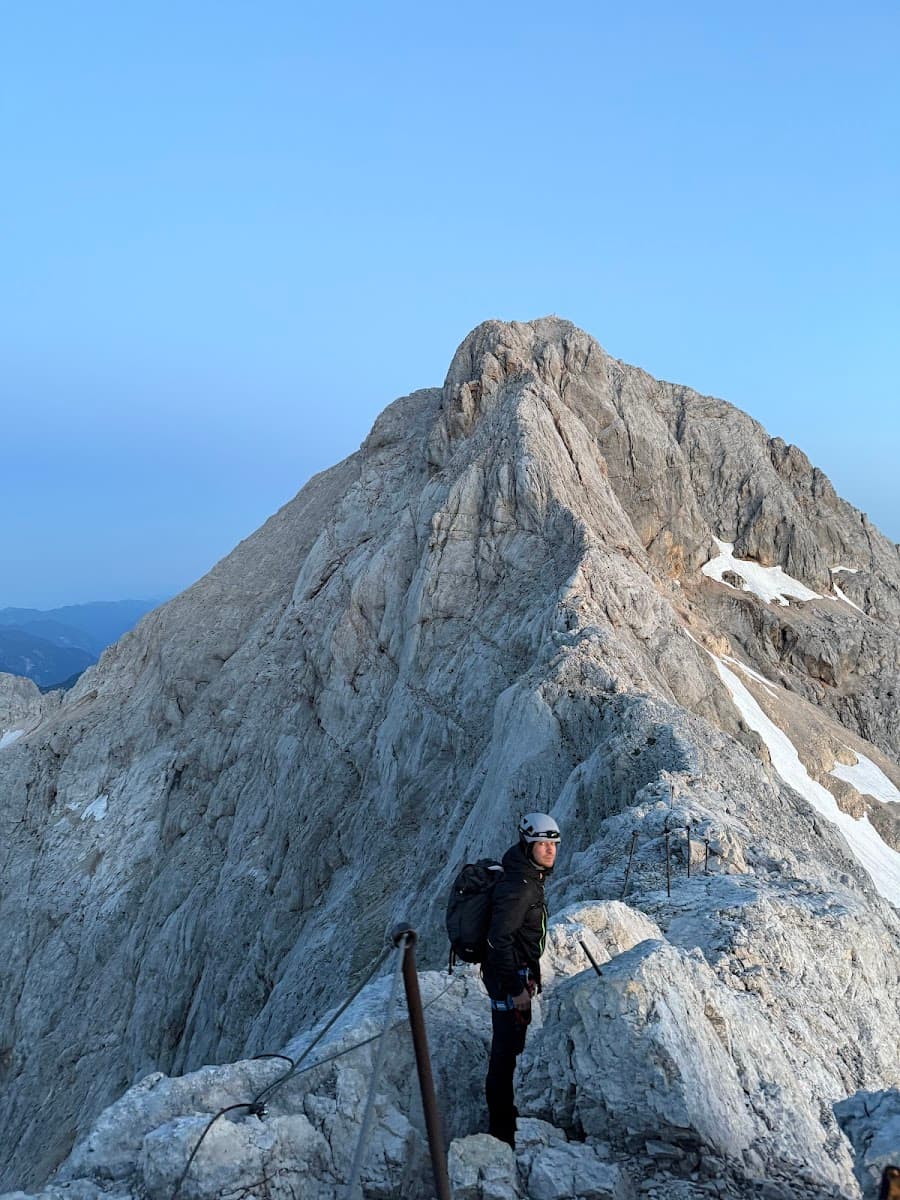Hiker with helmet and backpack on exposed rocky mountain ridge with via ferrata cables