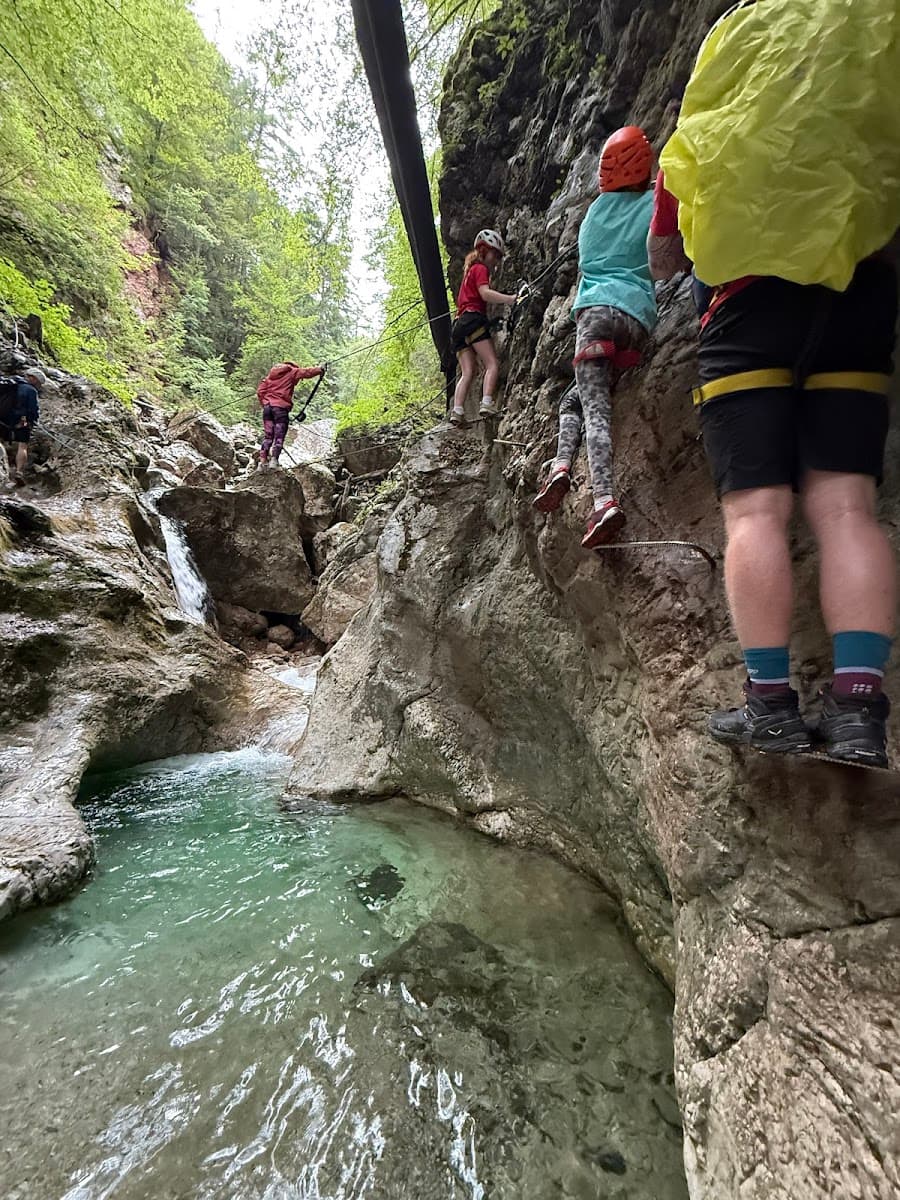 Canyoneering group climbing rocky gorge with clear turquoise water pool and small waterfall.