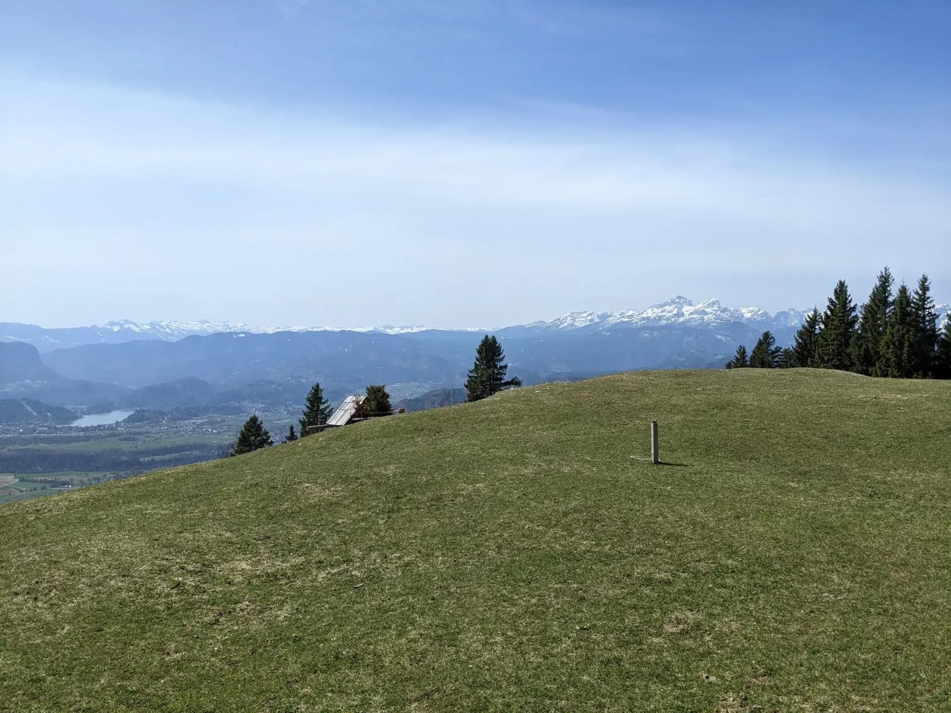 Grassy pasture hill overlooking valley with lake and snow-capped mountains in distance