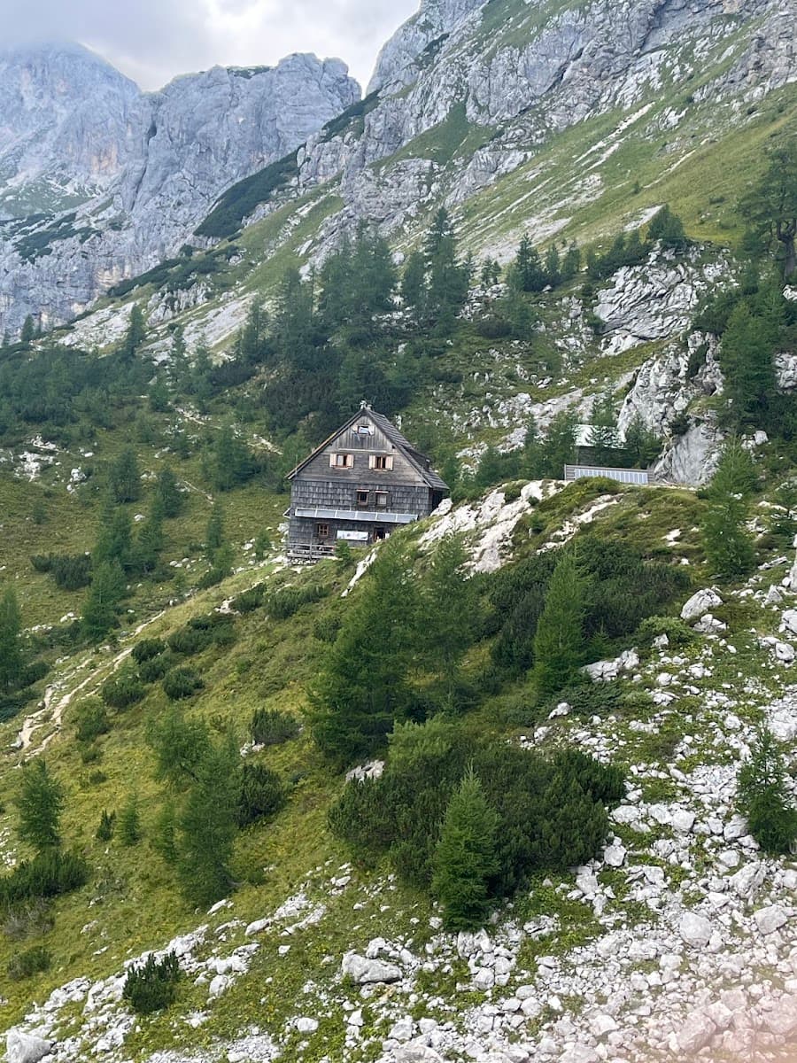 Wooden mountain hut nestled on a steep, grassy slope beneath rocky alpine peaks