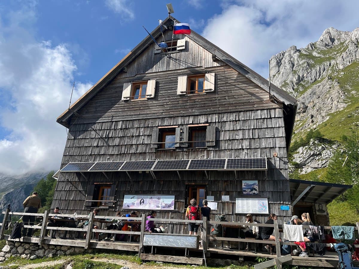 Wooden mountain hut with solar panels and hikers resting on the deck near rocky peaks.