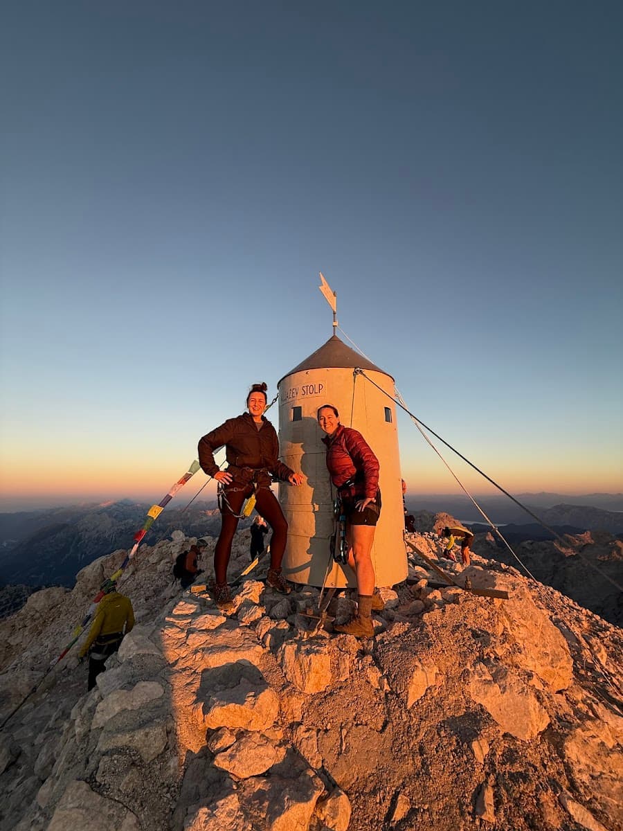 Hikers posing by the Triglav Stolp summit marker on rocky mountain peak at sunrise