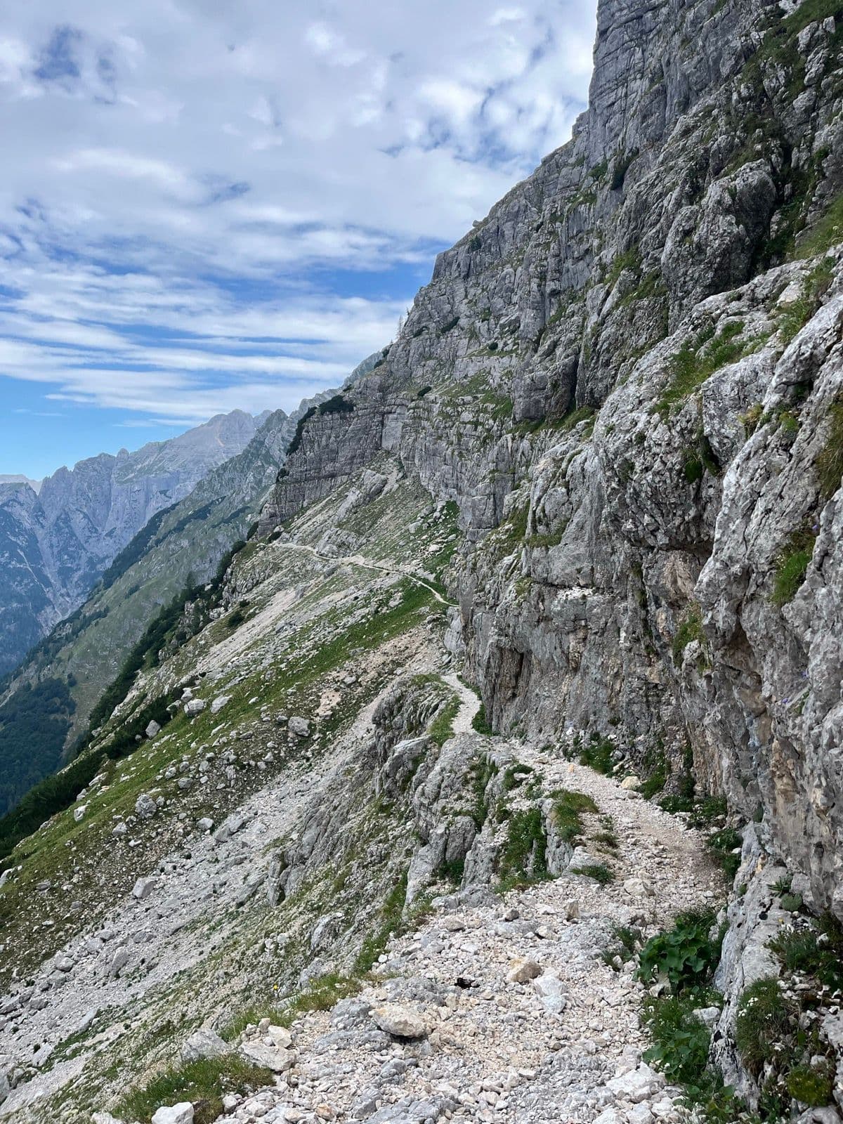 Narrow hiking trail carved into a steep rocky mountain slope with distant mountain peaks.