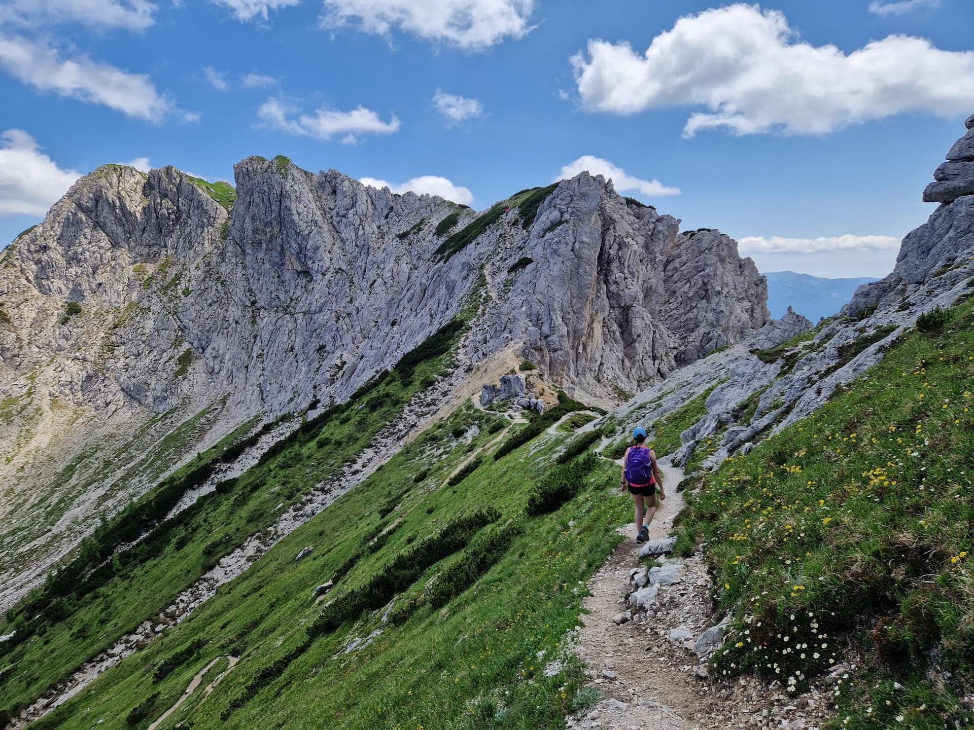 Hiker with a backpack walking on a trail through the jagged limestone peaks of Mount Triglav in the Julian Alps.