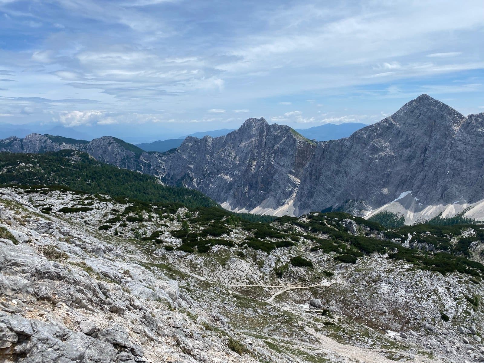 Rugged mountain peaks and rocky alpine terrain with a hiking trail under a cloudy sky.