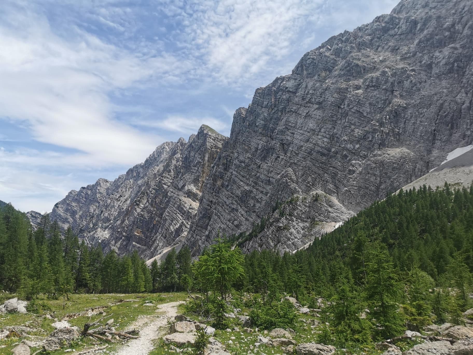 Steep limestone mountain face of Mount Triglav in the Julian Alps with a hiking trail and pine forest.