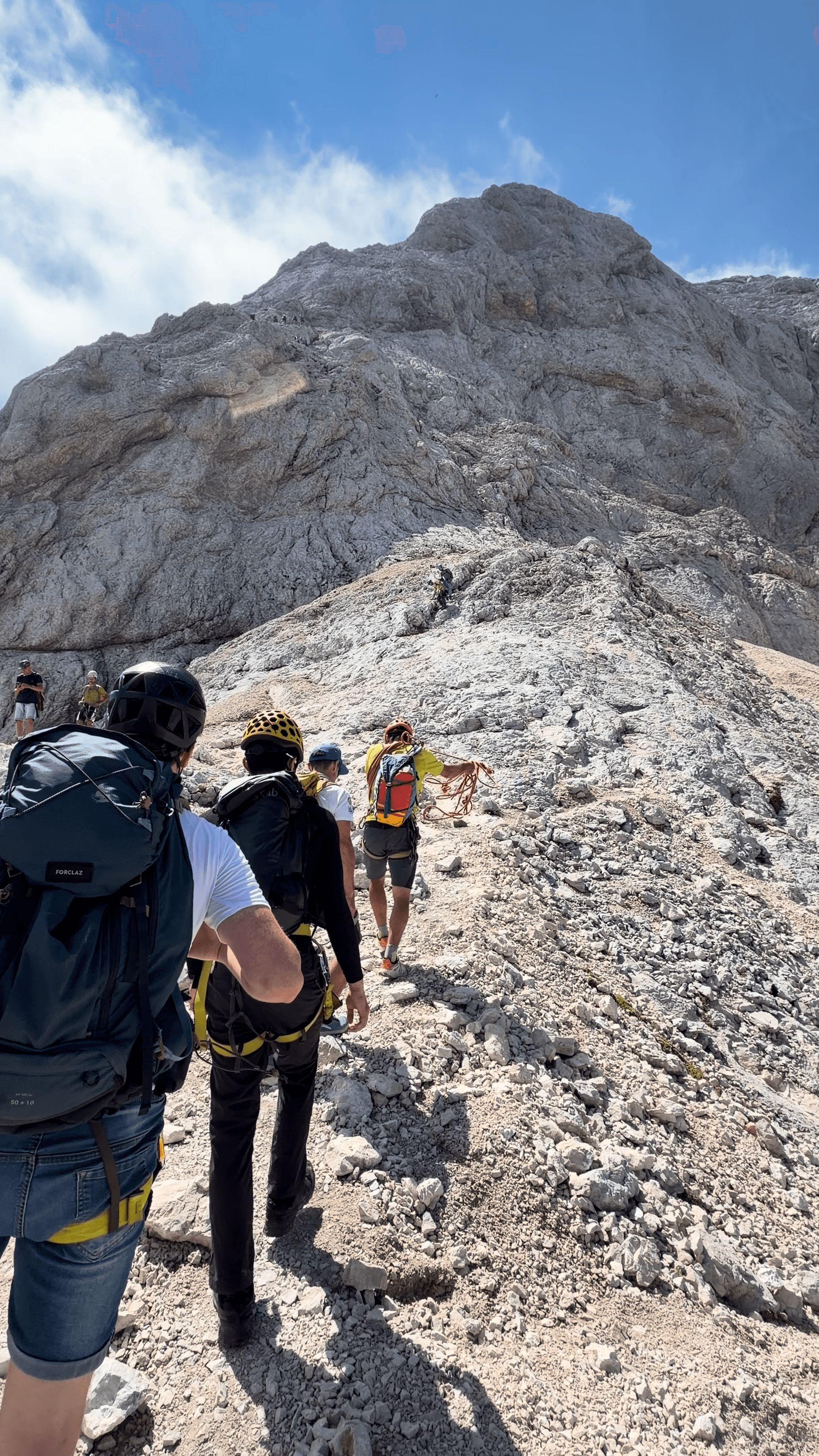Hikers climbing rocky mountain trail with helmets and backpacks