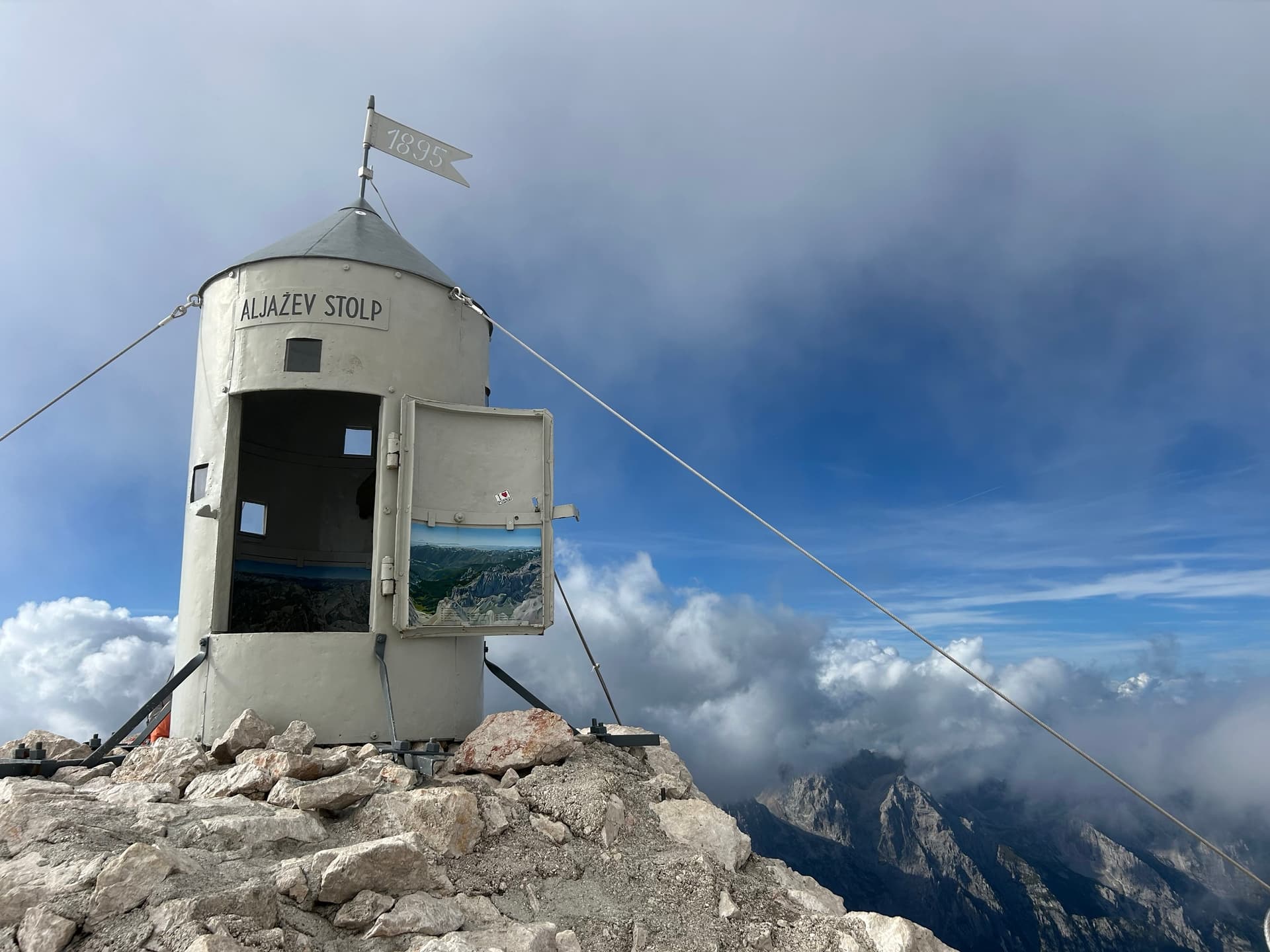 Aljaž Tower on the summit of Triglav mountain with cloudy sky and rocky peaks