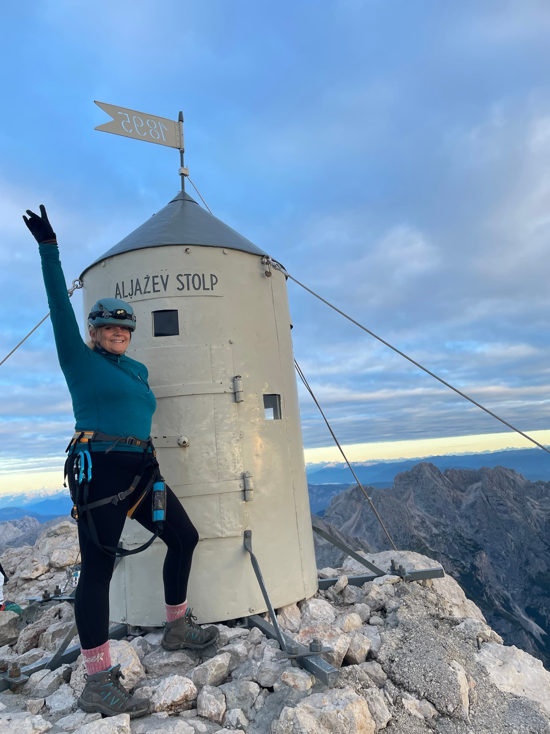 Hiker waving at the Aljaž Tower on Triglav summit with mountain background
