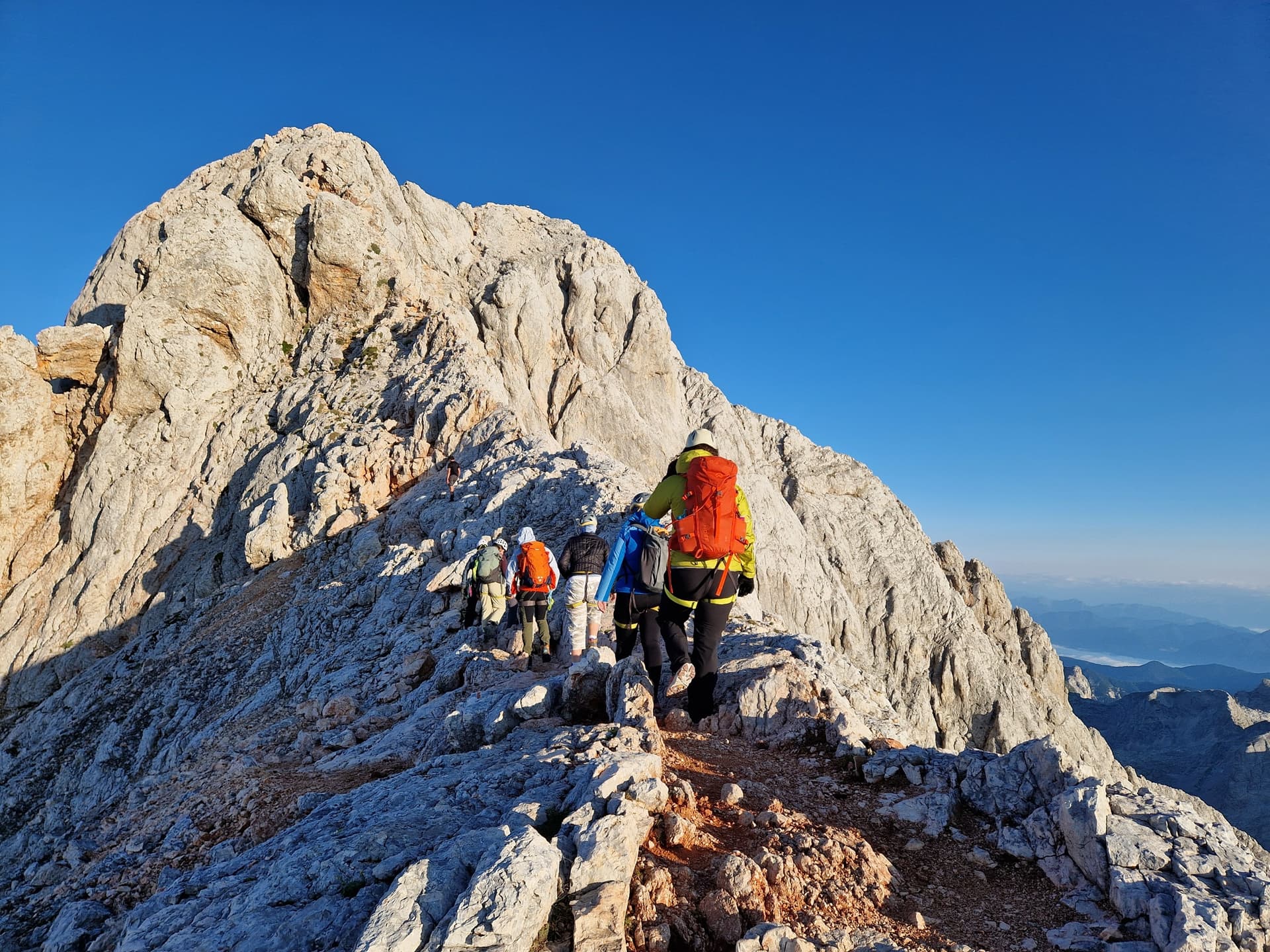 Roped climbers hiking on a rocky mountain summit ridge under a clear blue sky