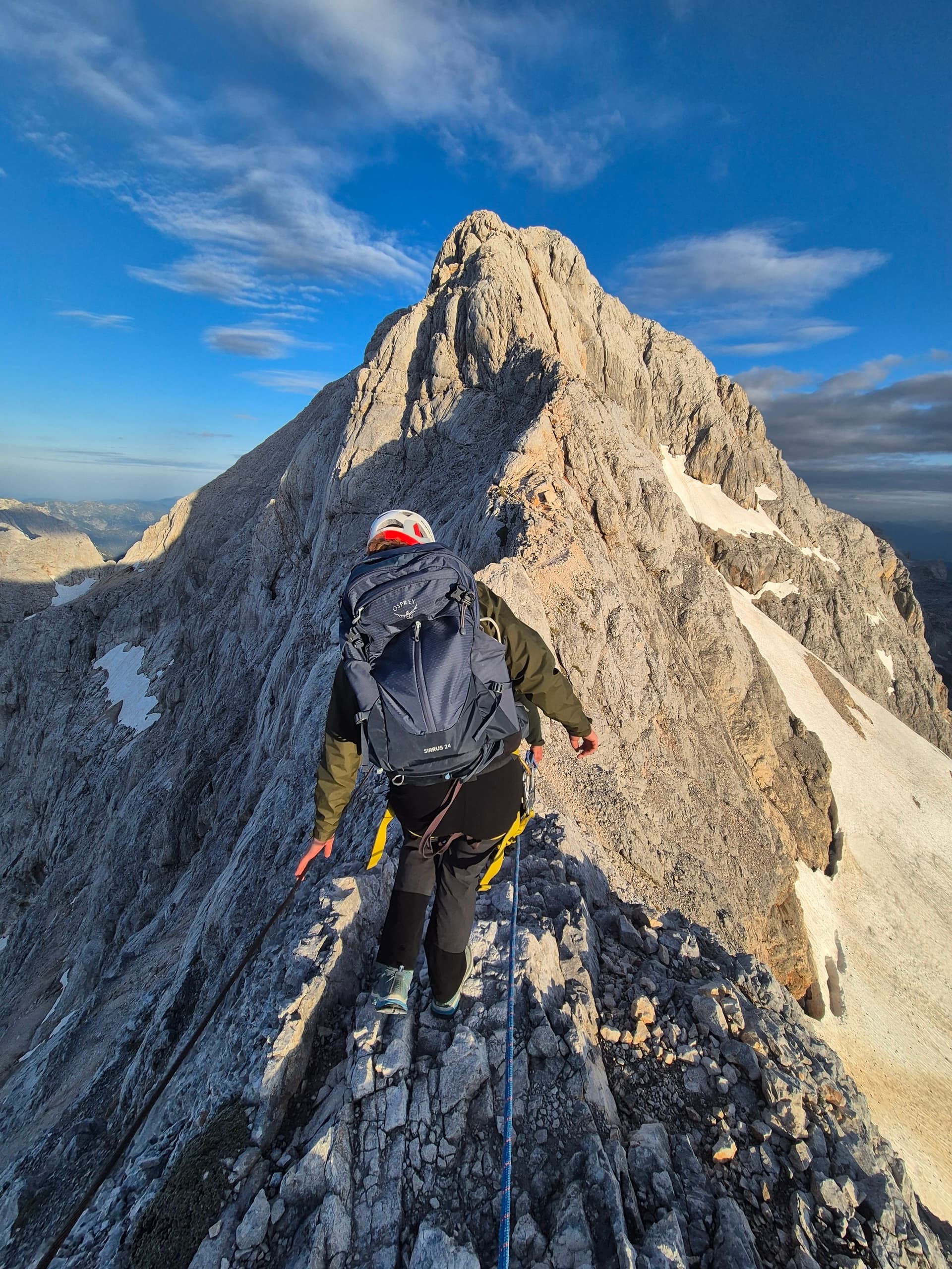 Climber hiking on a narrow limestone mountain crest with rope and backpack