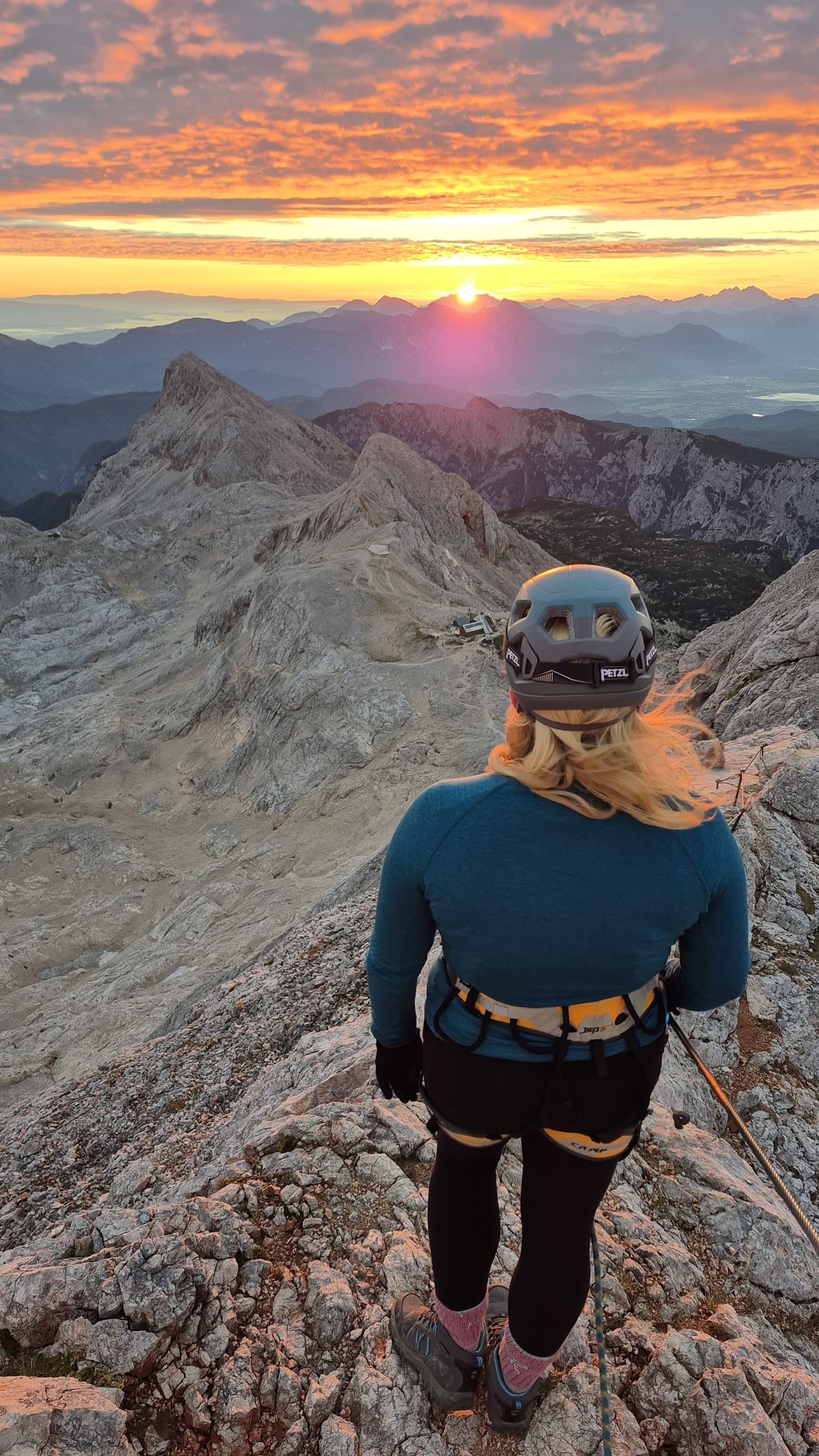 Hiker wearing helmet and climbing harness watching sunrise from mountain ridge