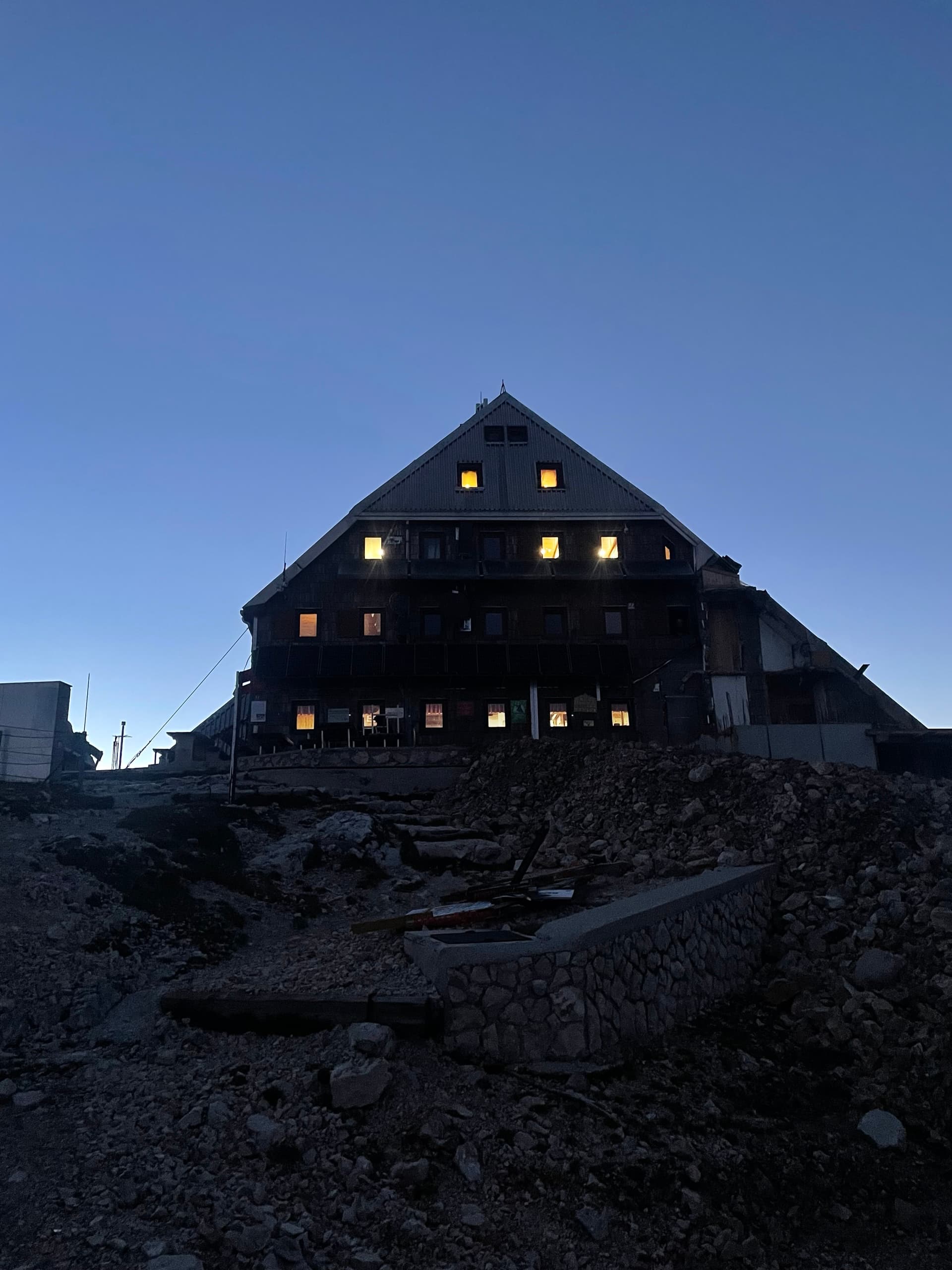 Mountain hut lit up at dusk with glowing windows on rocky terrain