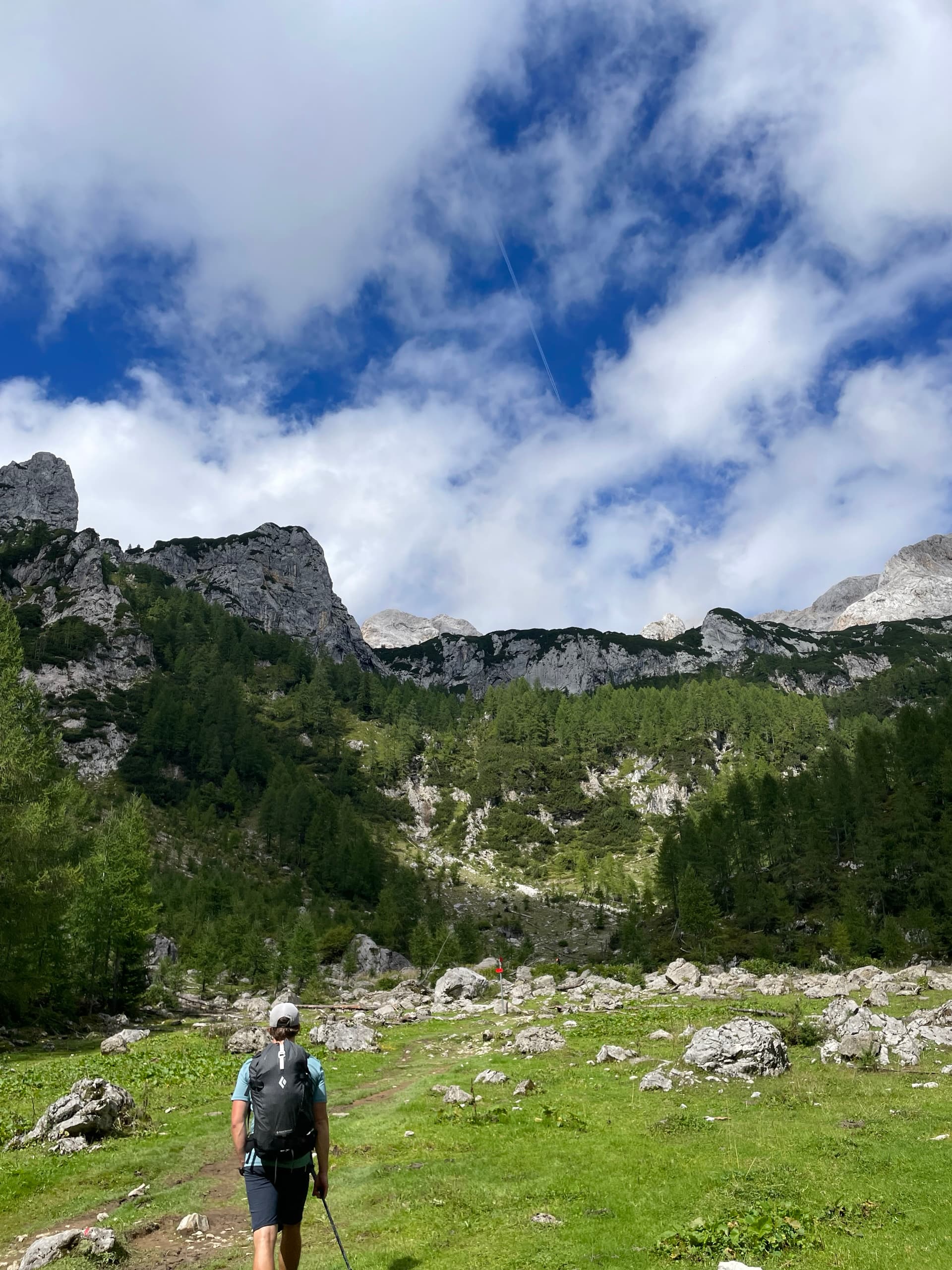 Hiker with backpack walking on mountain trail below limestone cliffs and pine forest