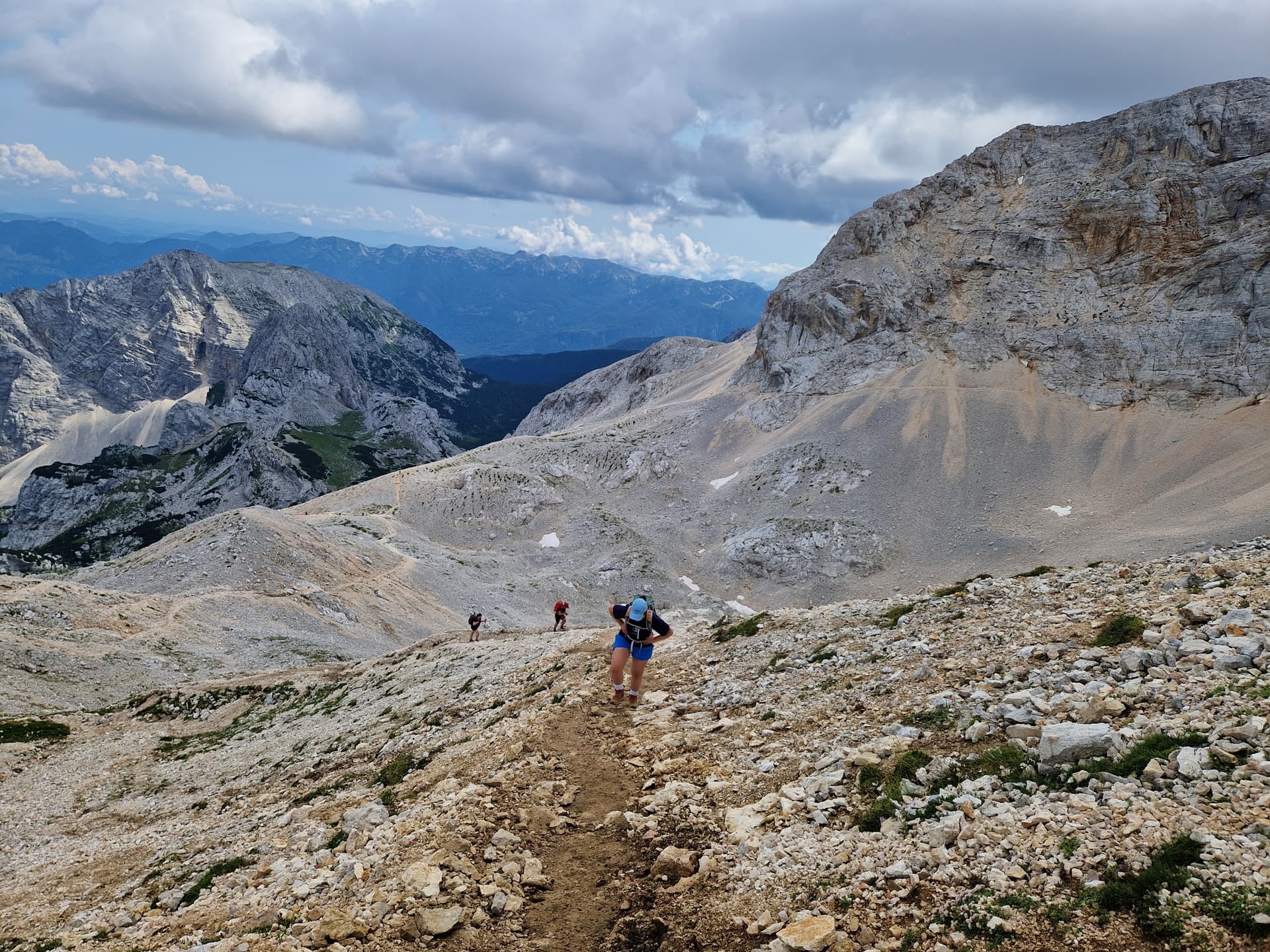 Hiker on a high scree trail in alpine mountains with cloudy sky