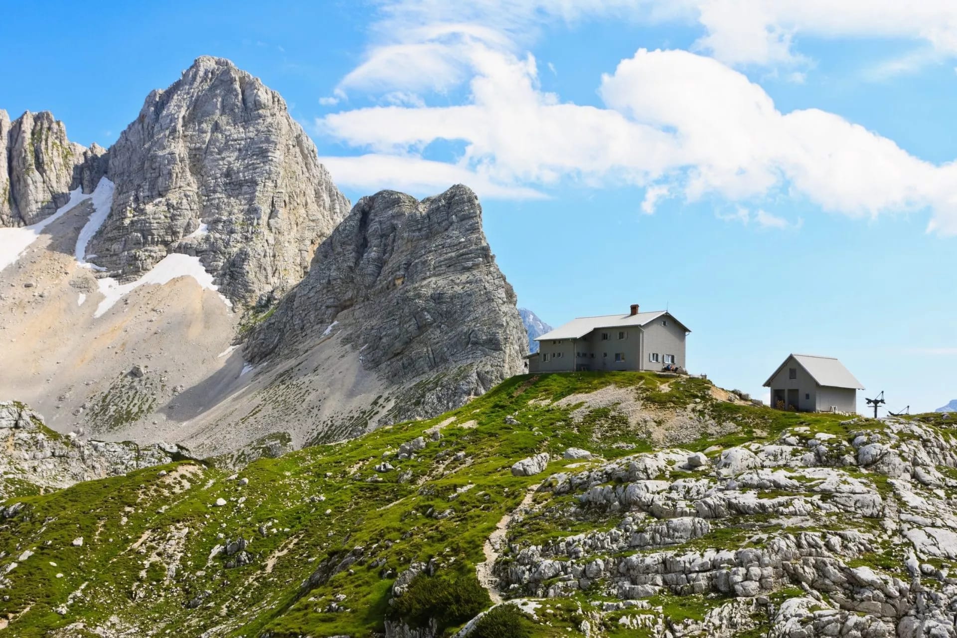 Pogacnik lodge on Kriski Podi with massive rocky mountains and summer snow patches