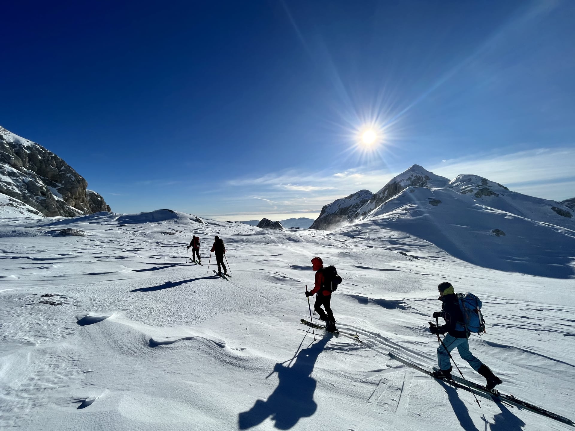 Ski touring on snow-covered alpine terrain under a bright sun near Kredarica.