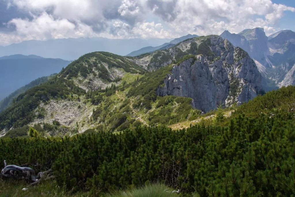 Mountain trail winding through green slopes and rocky peaks under a cloudy sky