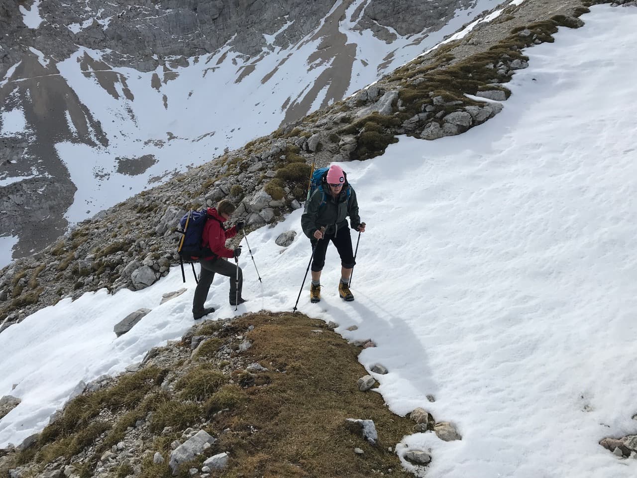 Hikers with trekking poles ascend a snowy, rocky alpine slope near Kredarica.