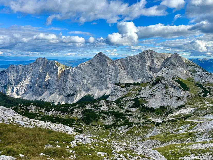Rugged, layered limestone mountains under a blue sky with white clouds, likely Triglav massif.