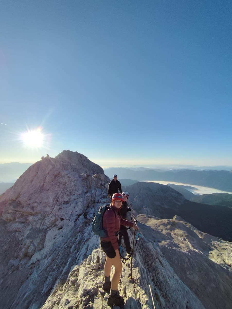 Hikers with helmets traversing a narrow, rocky mountain ridge under bright sun