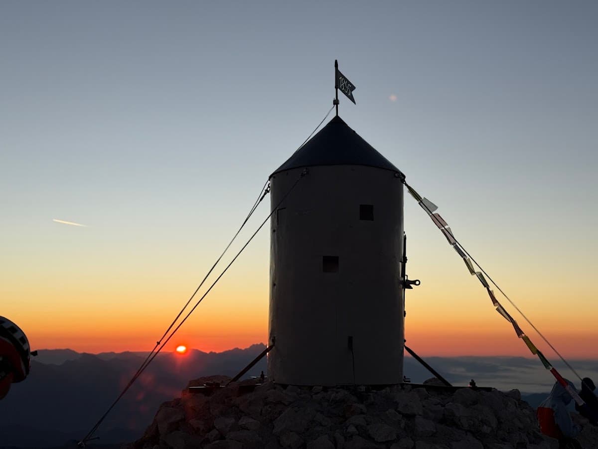 Cylindrical summit structure silhouetted against sunrise over distant mountain range