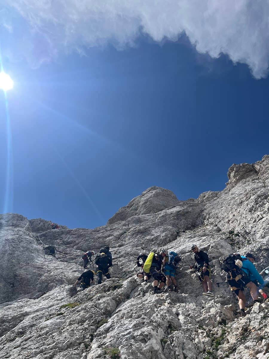Hikers climbing steep rocky mountain under bright sun and blue sky