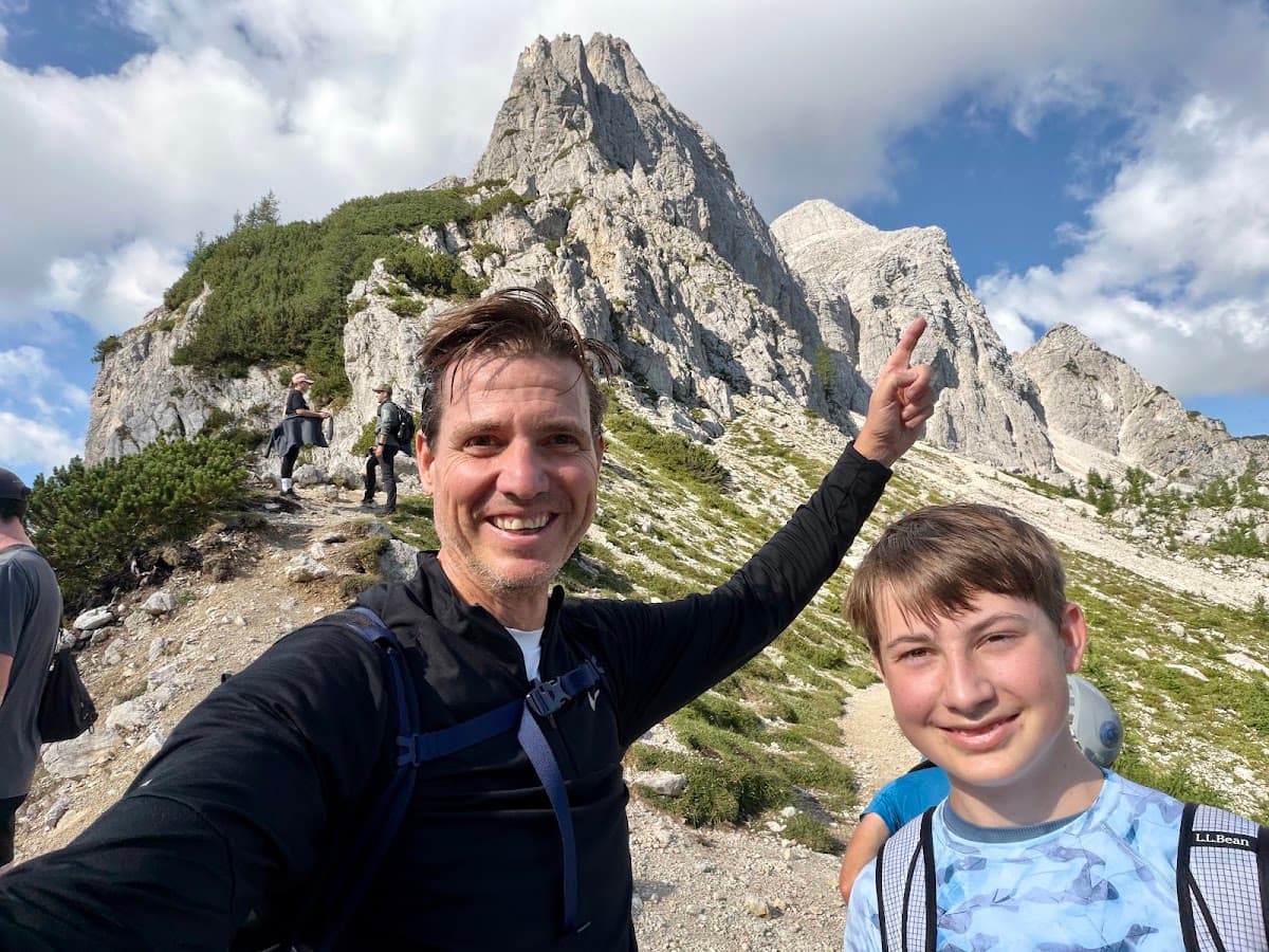 Hikers taking a selfie on a rocky mountain trail with alpine peaks