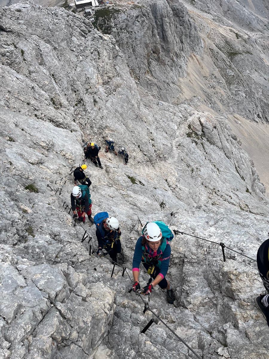 Hikers climbing steep rocky mountain terrain using safety cables and harnesses