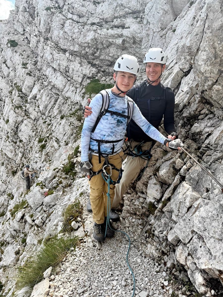 Two people wearing helmets and climbing harnesses on a rocky mountain via ferrata route