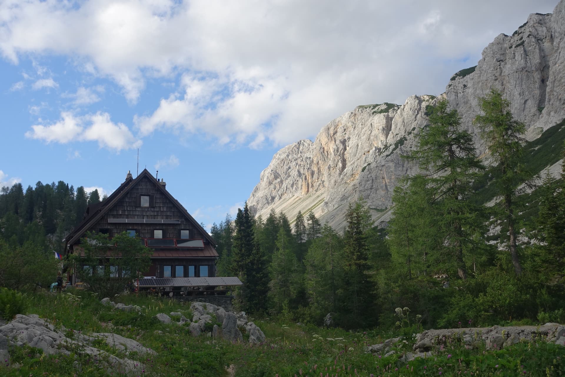 Wooden mountain hut nestled below towering limestone cliffs and pine trees