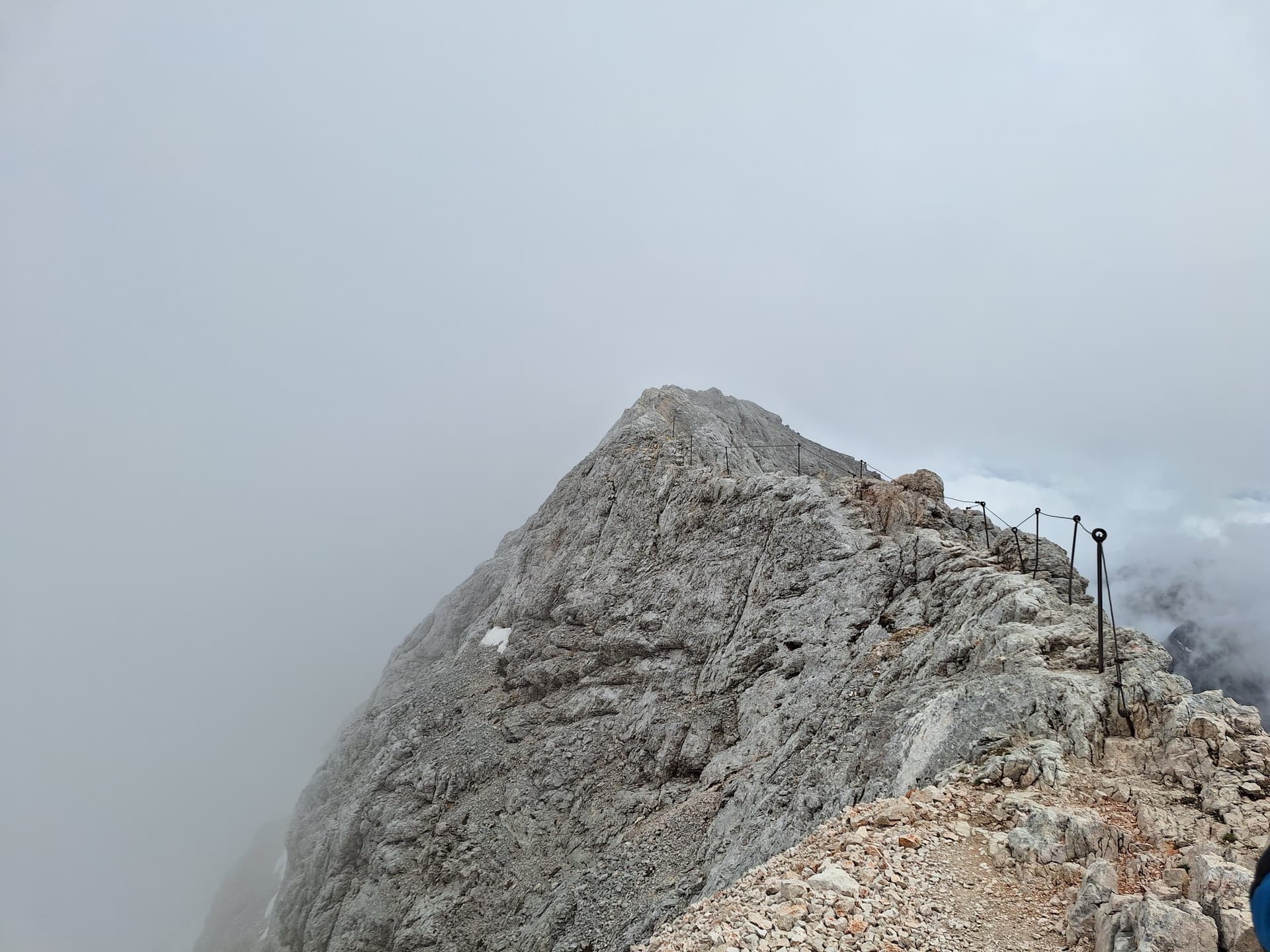 Rocky mountain summit ridge with safety cables and posts in thick cloud