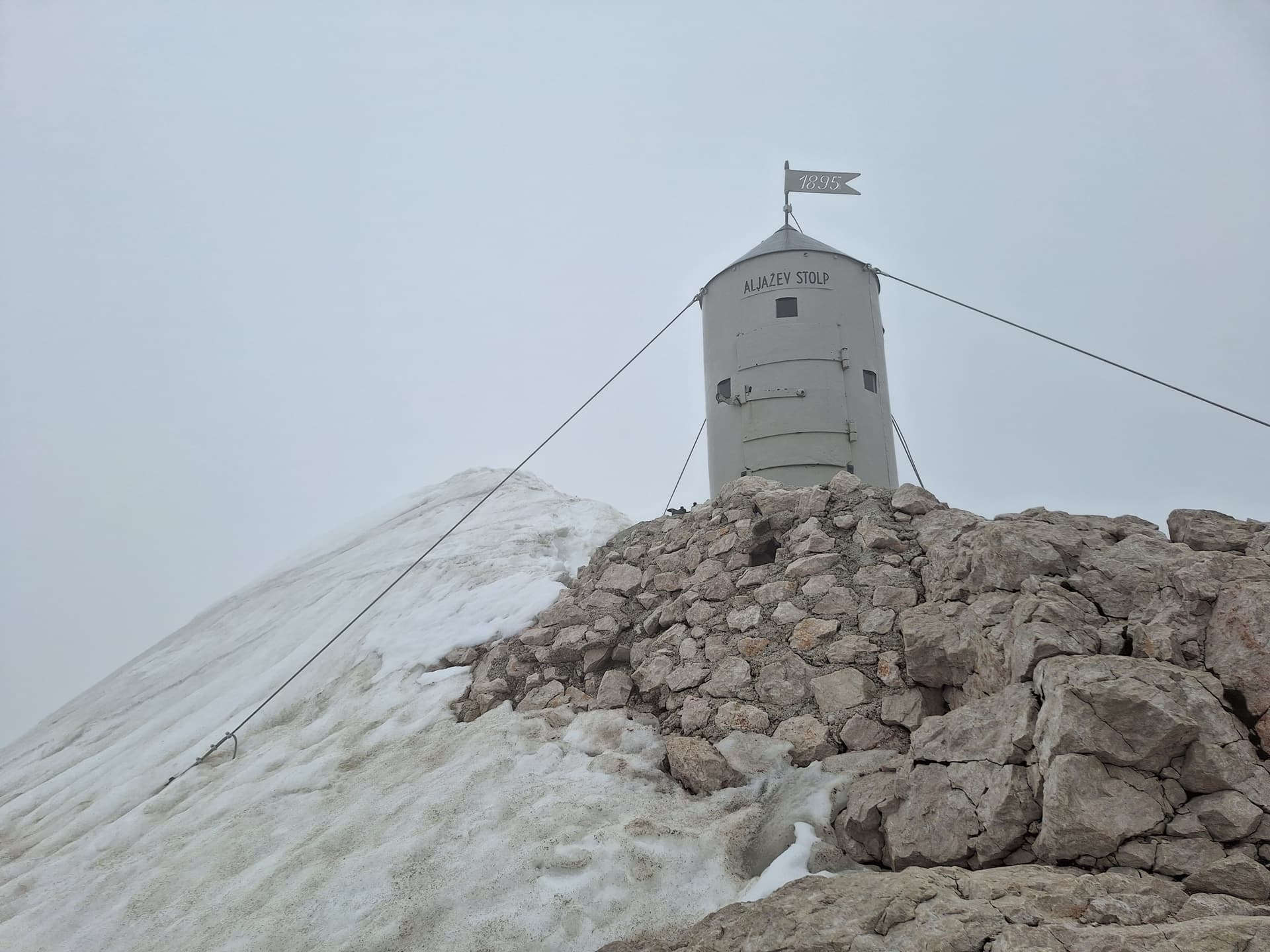 Aljažev Stolp tower on snowy mountain summit with rocky terrain