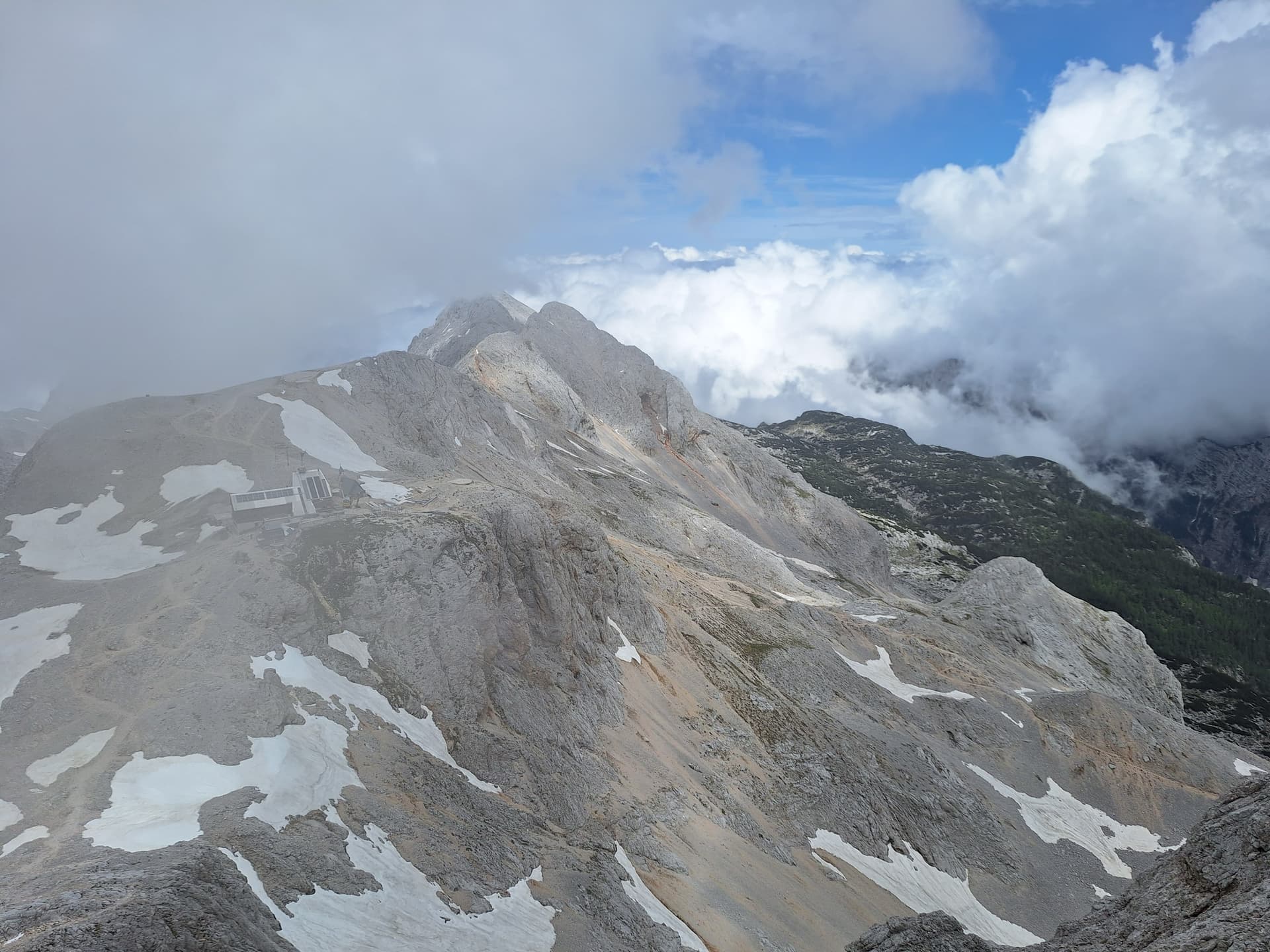 Alpine limestone slopes with patches of snow and clouds wrapping around mountain peaks