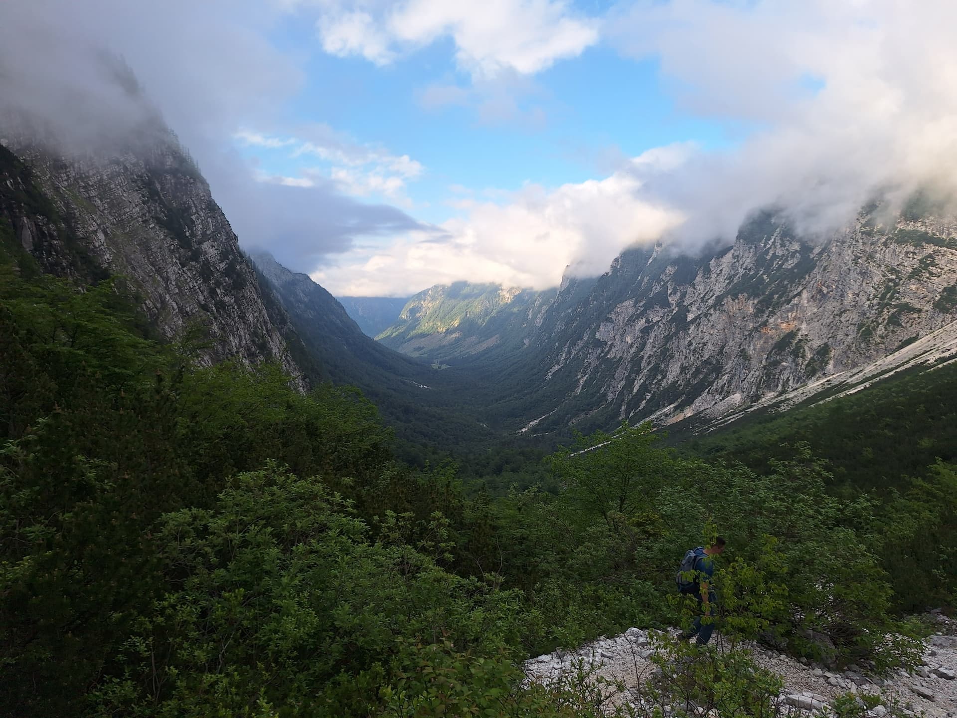Hiker walking on mountain trail in green valley between high rocky walls